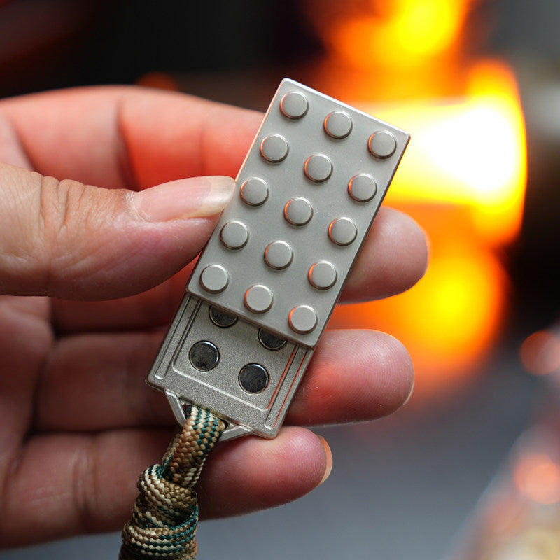 Metal Building Block slider held partly open, showing raised studs, internal circular inserts and a cord at its end.