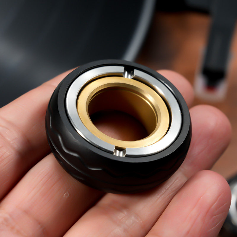 Black Style D ring with a wavy outer band, silver-tone face and gold-tone inner ring, held in a hand.