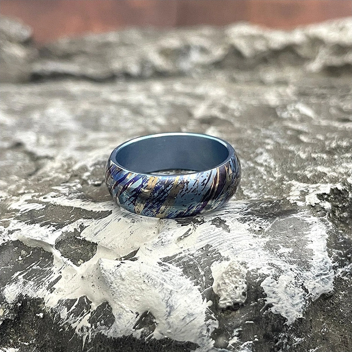 Anodized Titanium Band Ring: blue streak patterned ring resting on stone (gallery view 03).