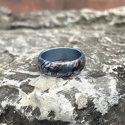 Anodized Titanium Band Ring: blue streak patterned ring resting on stone (gallery view 03).
