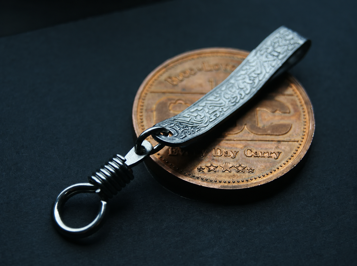 Silver-tone scroll-patterned EDC pocket clip with coiled connector and ring; display coin not included