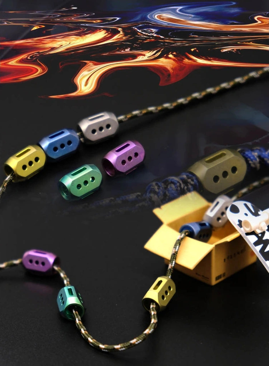 Nine-Star TC4 Titanium Lanyard Bead: colored faceted beads beside a patterned tool prop (gallery view 03).
