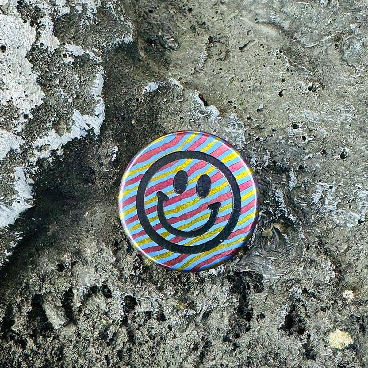 Smiley Face Titanium Lanyard Bead: striped smiley face resting on stone (gallery view 03).