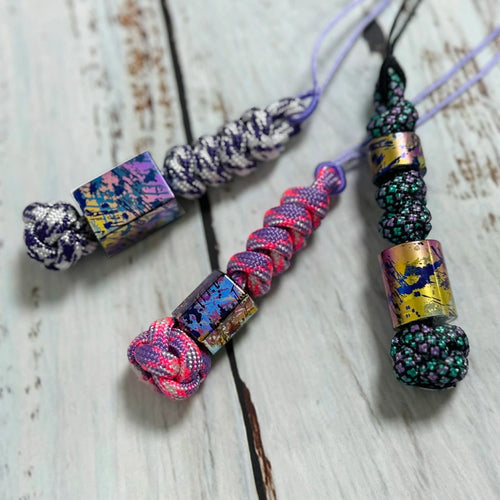 Classic Splatter Titanium Lanyard Beads: three splatter bead lanyards on pale wood (gallery view 01).
