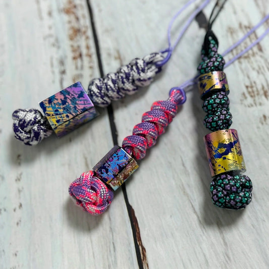 Classic Splatter Titanium Lanyard Beads: three splatter bead lanyards on pale wood (gallery view 01).