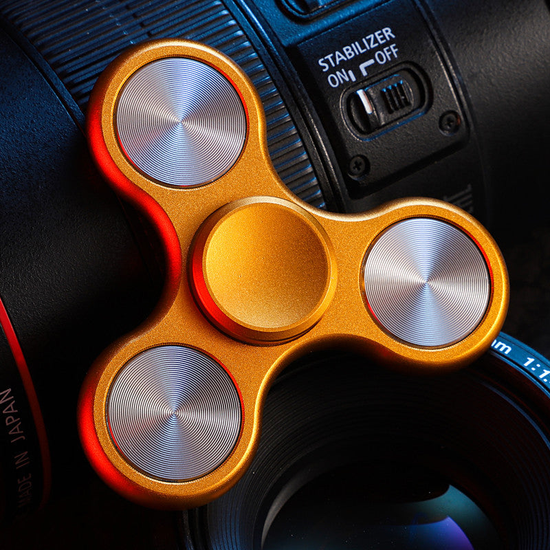 Gold-tone three-lobe spinner with silver-tone circular inlays; background camera is a photo prop.