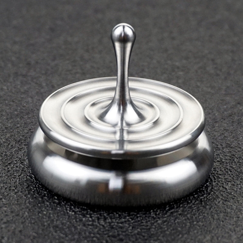 Silver spinning top with concentric ripple rings resting on a rounded metal base.
