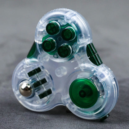 Clear three-lobed triangular fidget toy with green controls and a metal-colored ball beside three wheels.