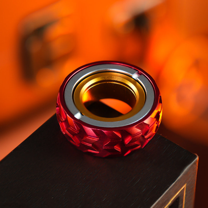 Red tire-pattern ring with a silver-tone face and gold-tone inner ring, shown on a dark block.